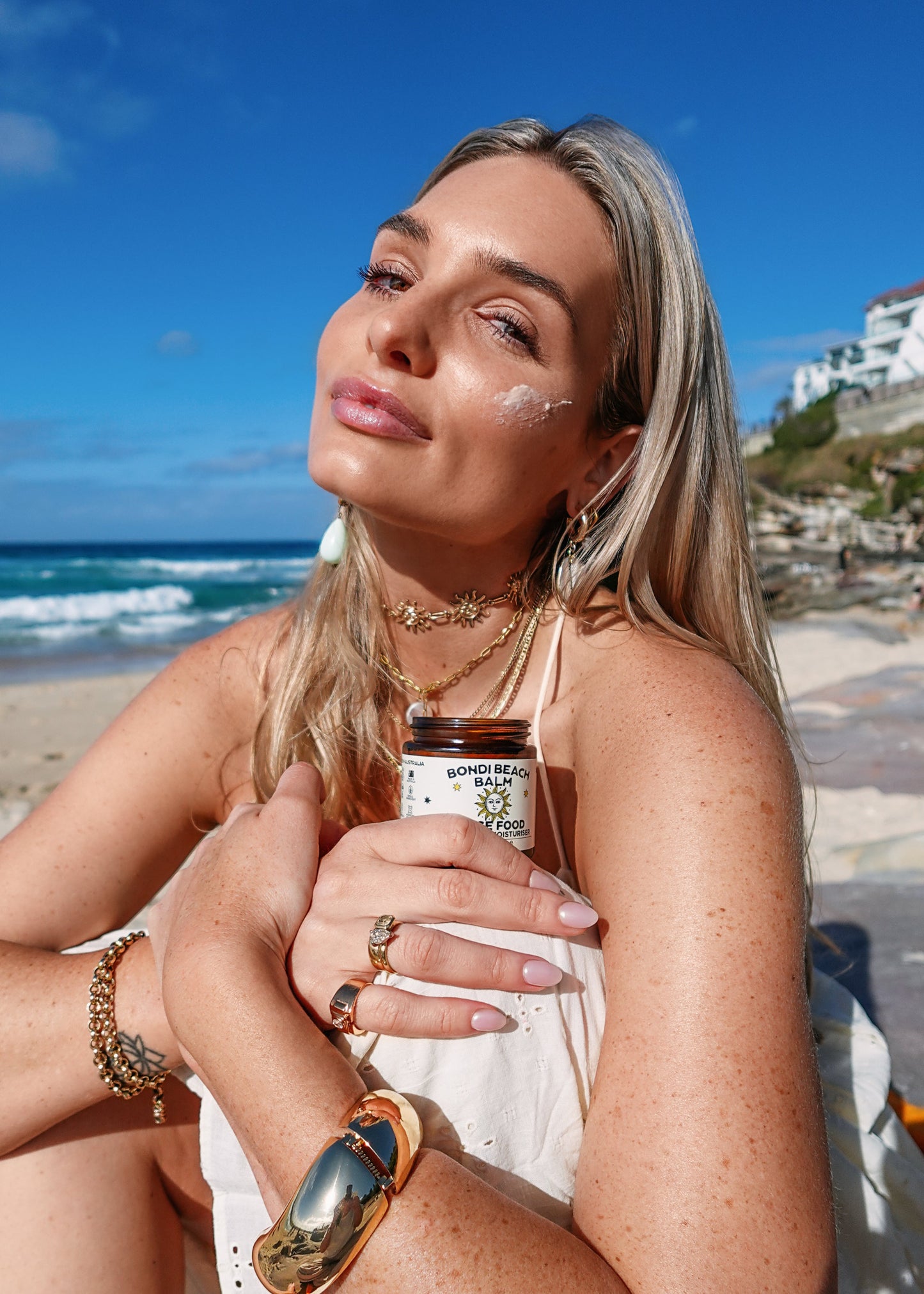 Woman on a beach holding a jar of 'Bondi Beach Balm' Face Food balm
