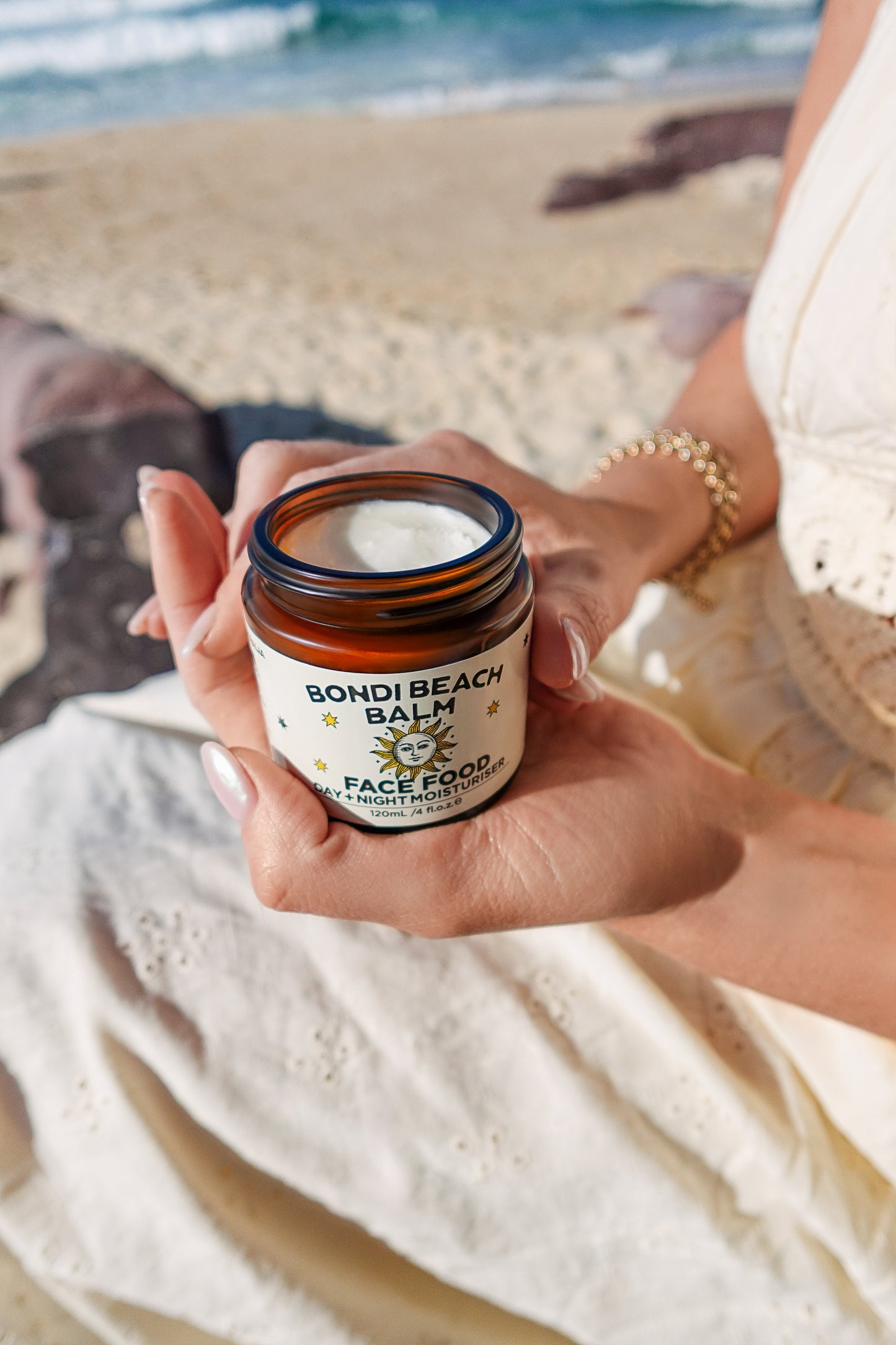 Person holding a jar of Face Food by Bondi Beach Balm on a beach.