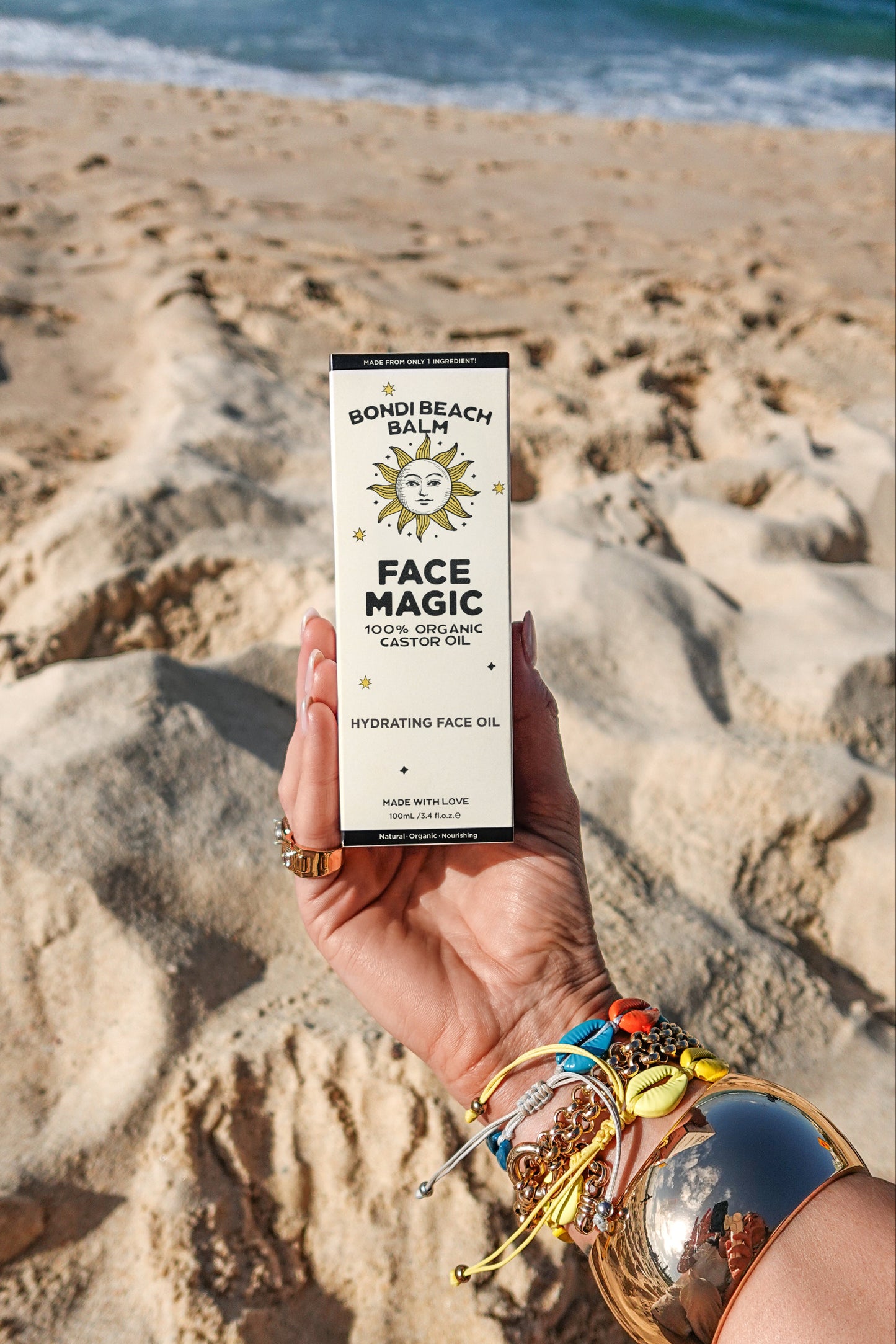 Hand holding a product labeled 'Face Magic' on a sandy beach.
