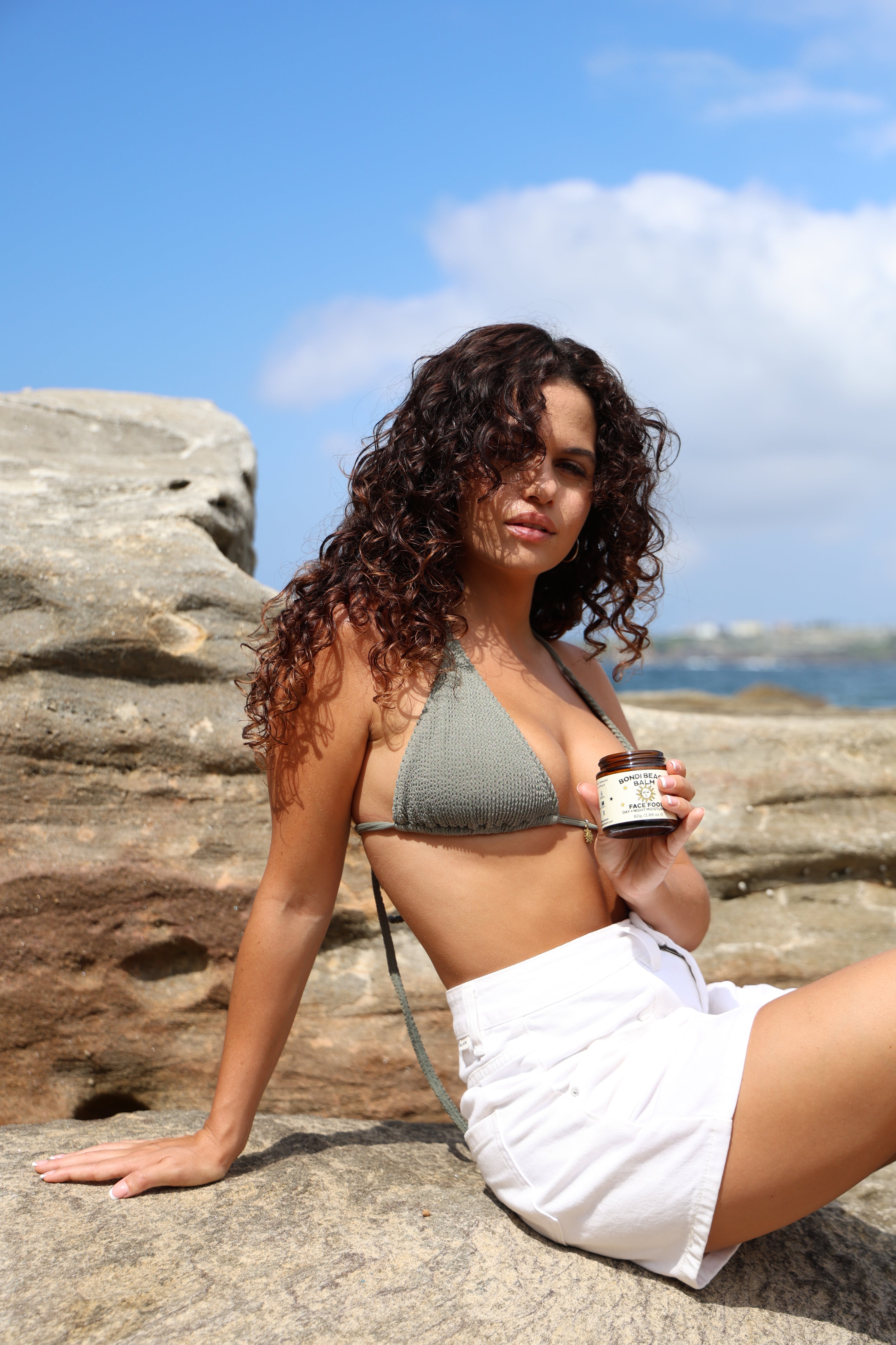 Woman holding a bottle against a stone wall with a blue sky background