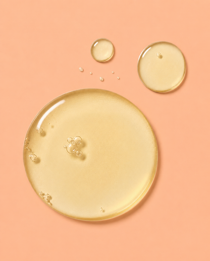 A glossy, translucent droplet of pale yellow rosehip oil or serum on a solid peach-pink background, with two smaller droplets above it.