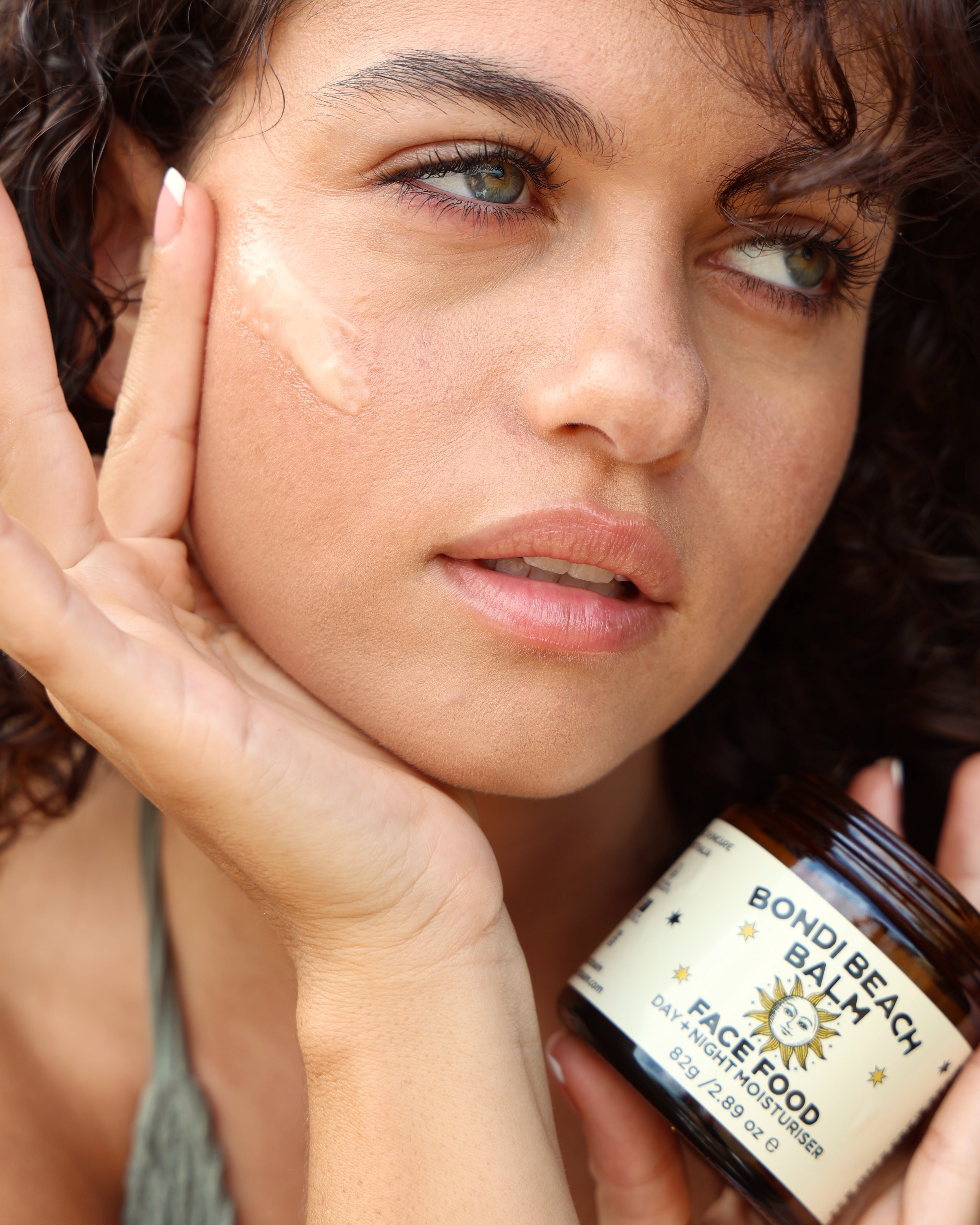 Woman holding a jar of 'Boho Beach Balm' by Face Food close to her face.